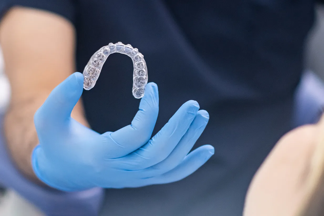 Hand wearing blue glove holding a clear dental aligner.