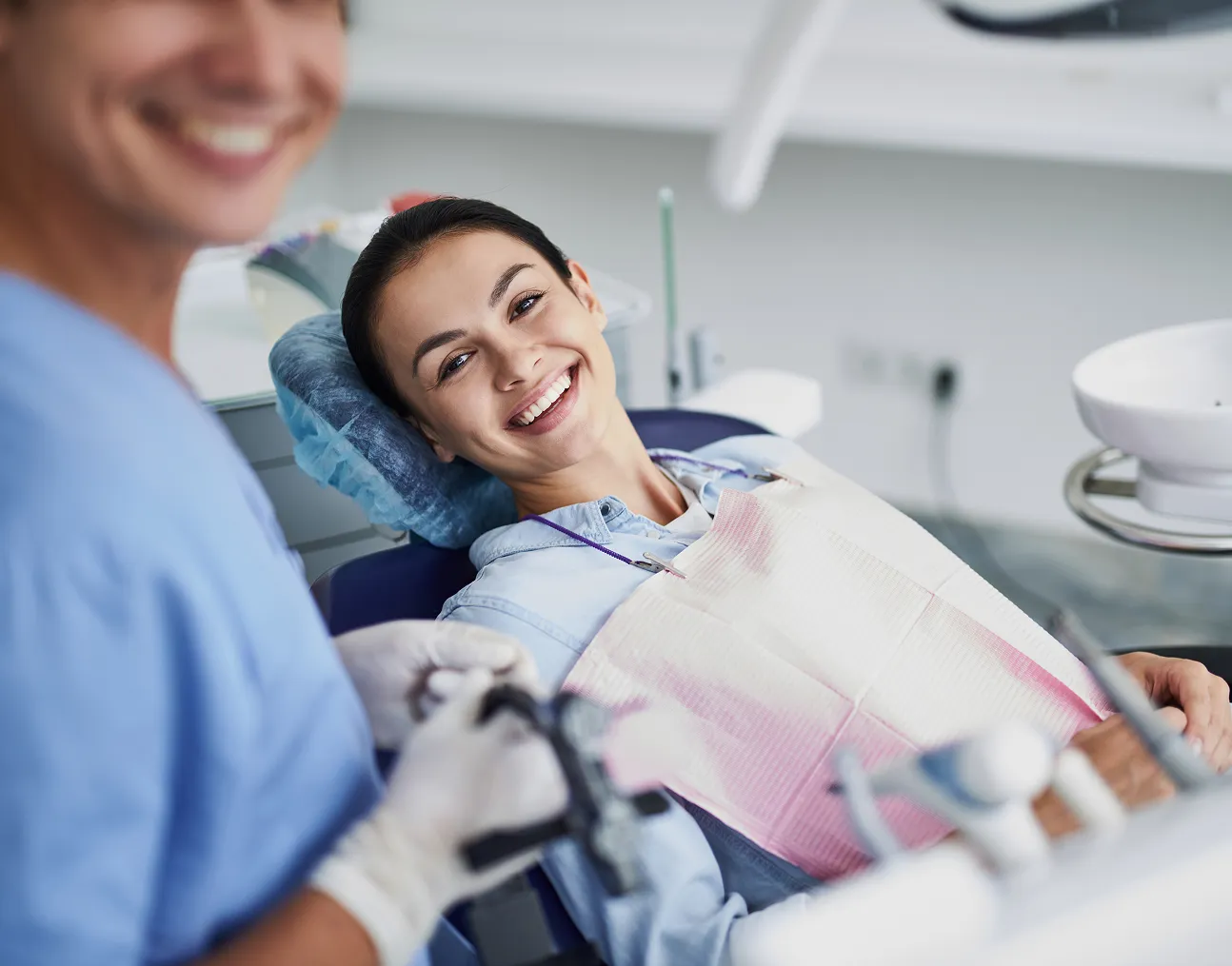 Smiling woman reclined in a dental chair with a protective bib, looking at a smiling dentist.