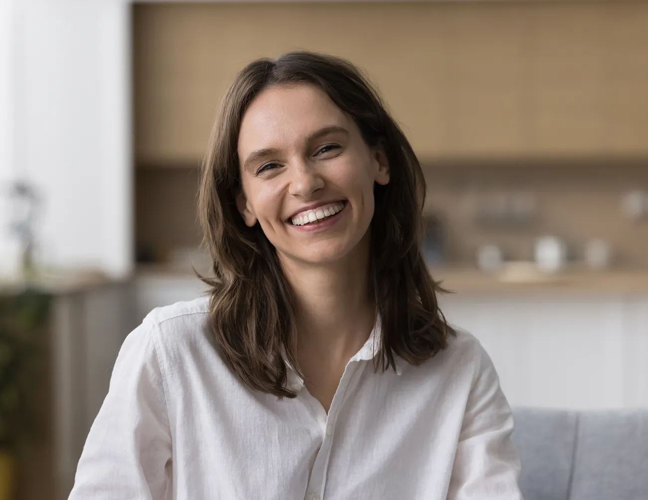 Smiling woman with brown hair wearing a white shirt seated indoors.