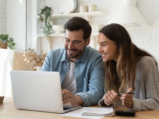 Smiling man and woman working together on a laptop at a table with papers and a calculator.