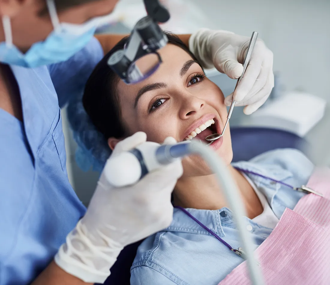 Woman smiling during a dental checkup with a dentist using dental tools.
