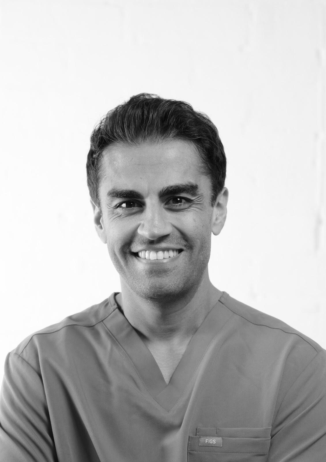 Smiling man in medical scrubs with short dark hair against a plain light background.