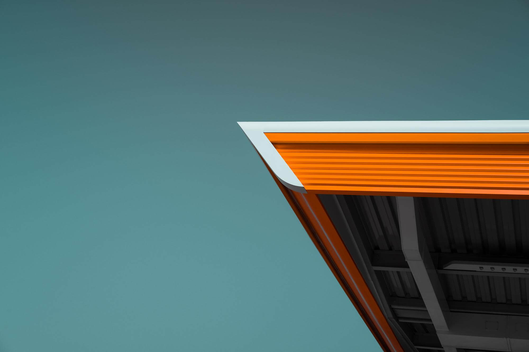 Close-up of modern building roof corner with orange and white trim against a clear blue sky.