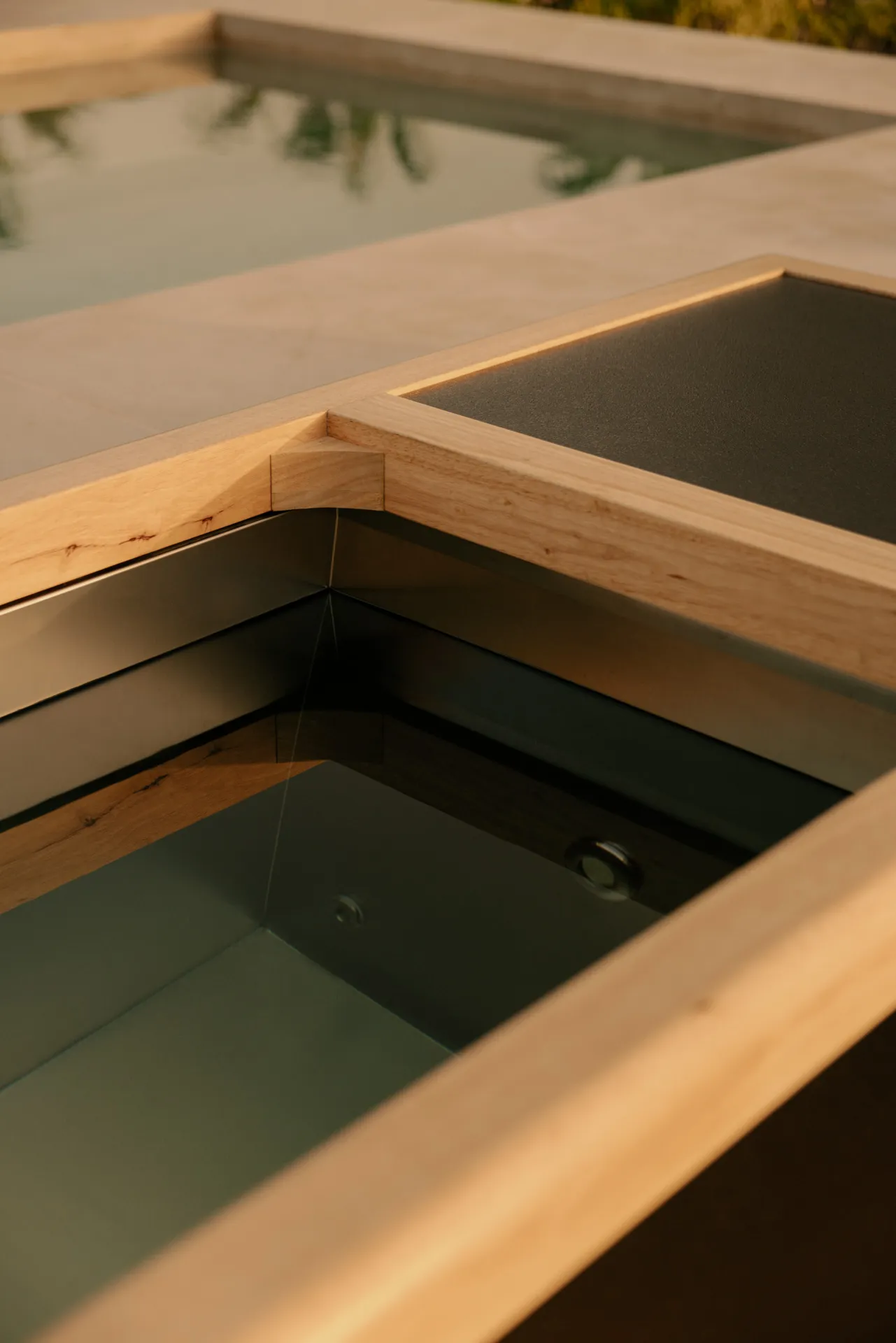 Close-up of a modern rectangular hot tub with wood trim and water inside, next to a tiled pool edge.