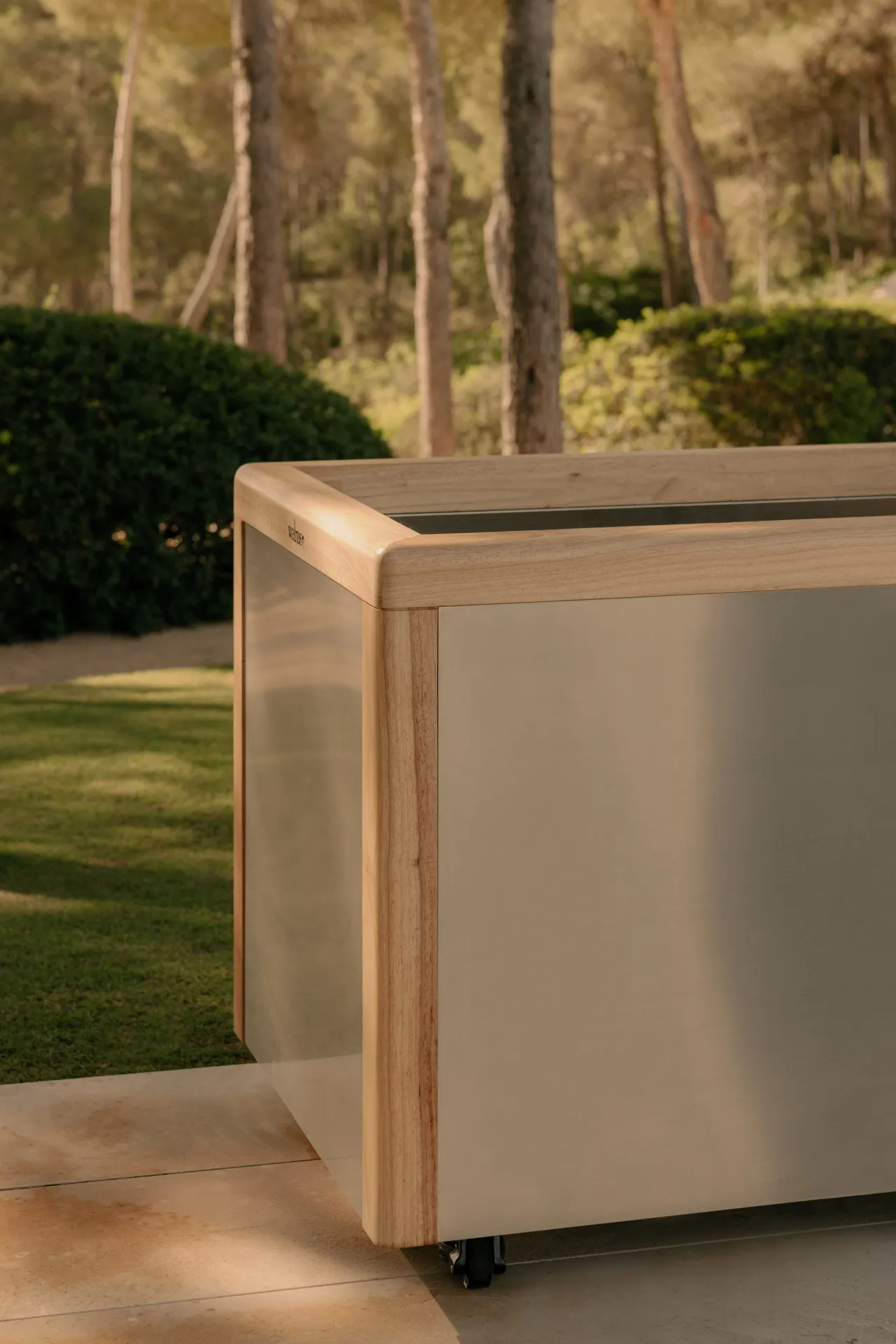 Close-up of a modern, rectangular wooden and metal planter box on wheels outdoors.