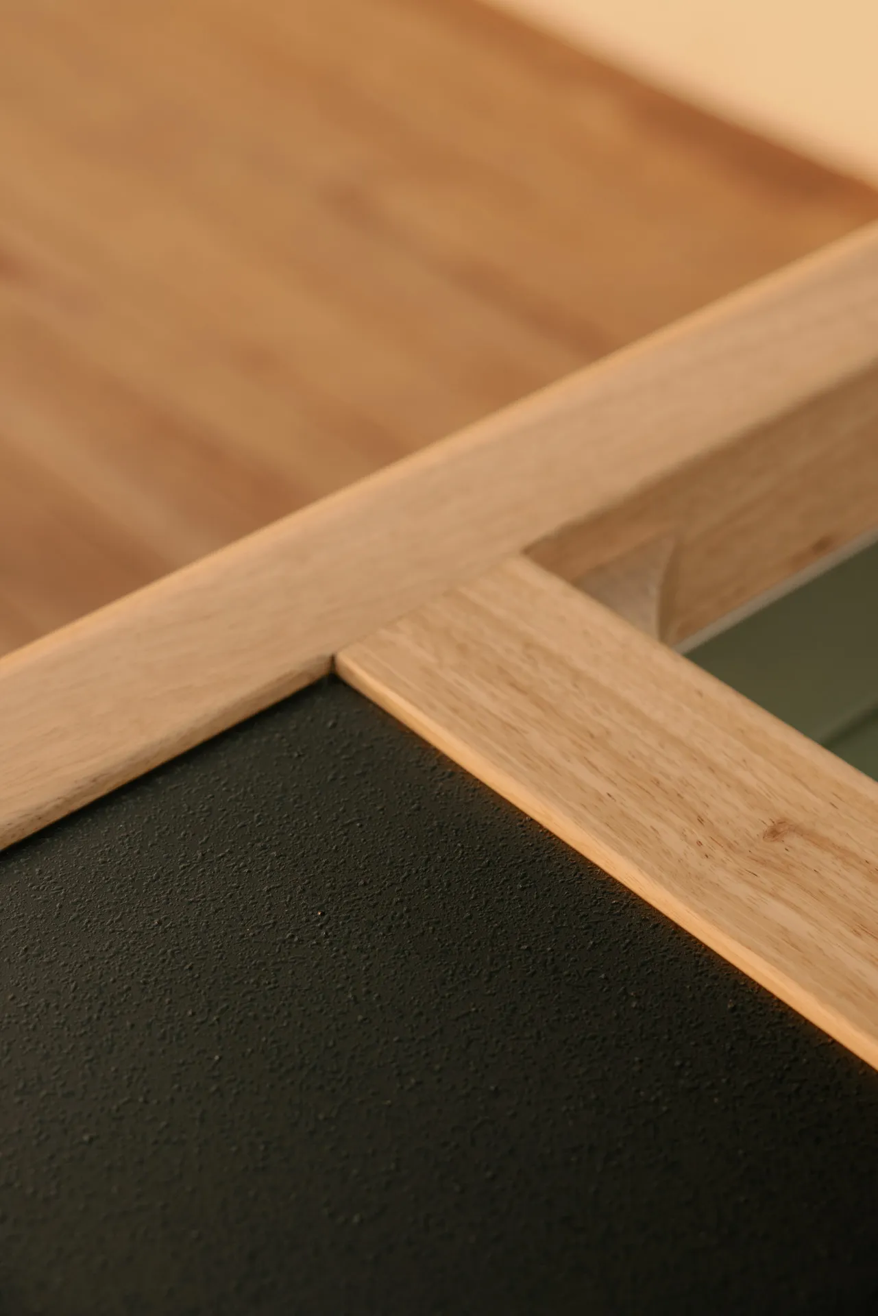 Close-up of a wooden table corner with a textured black surface and light wood frame.