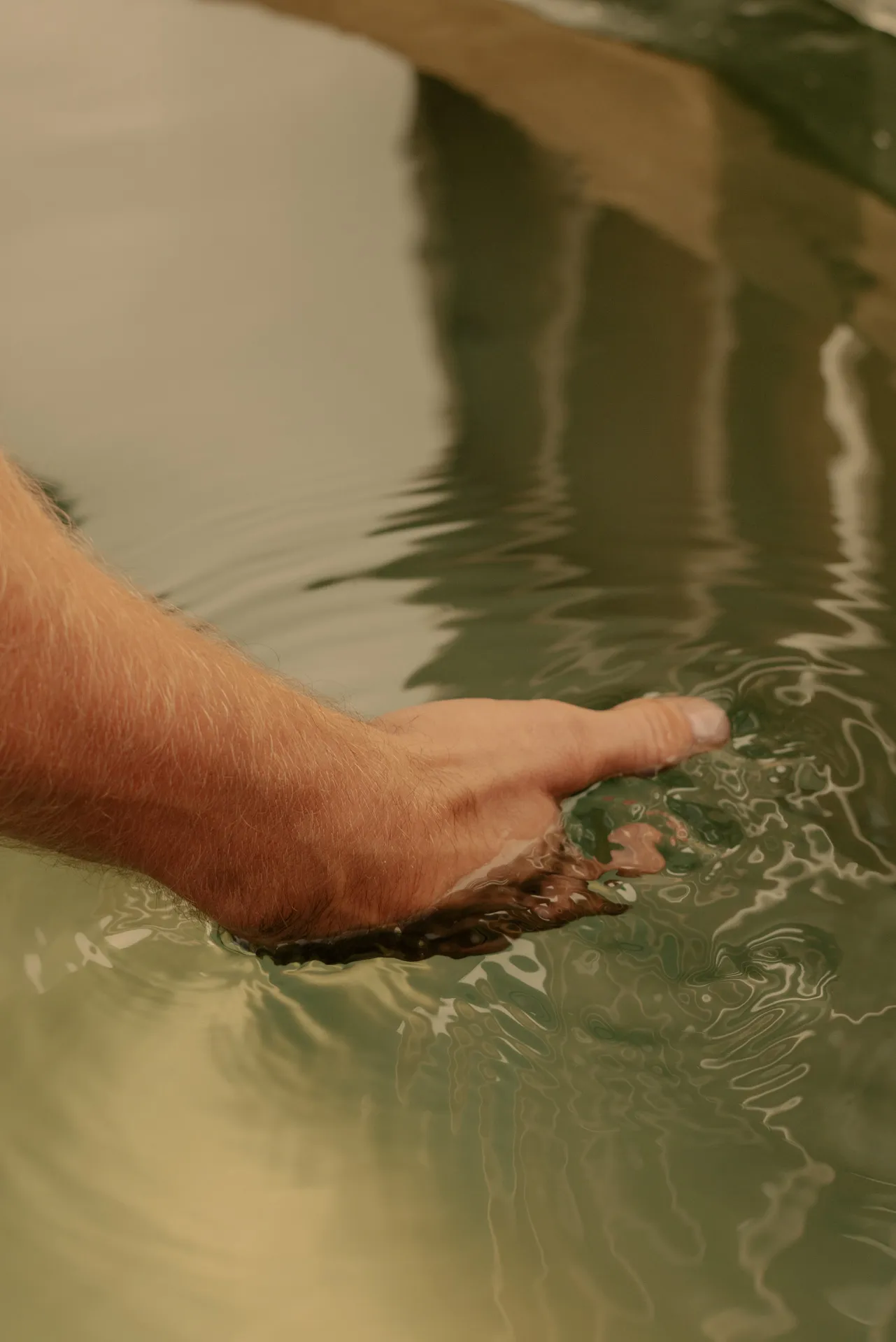 Close-up of a hand gently touching the surface of calm water creating small ripples.