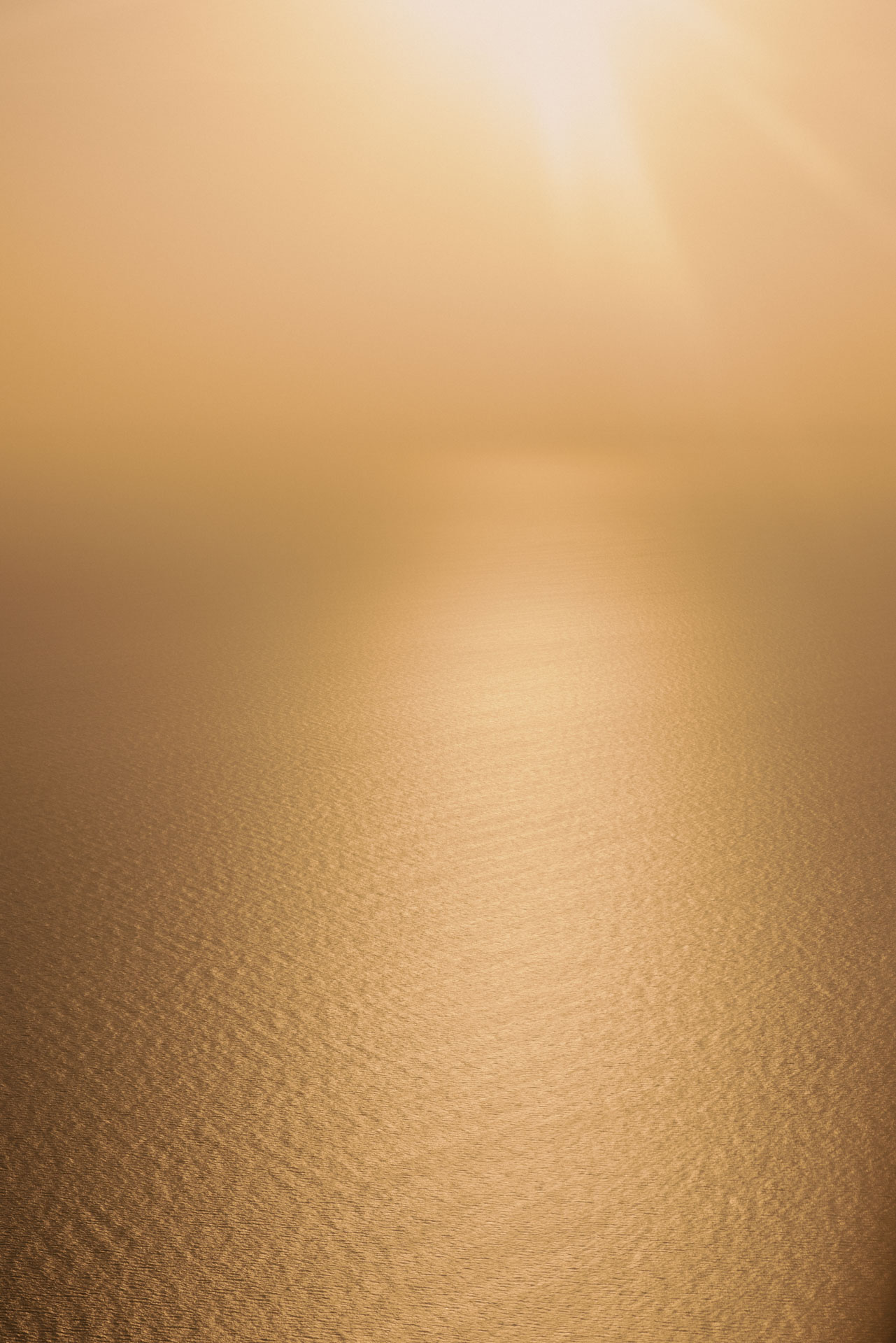 Golden sunlight reflecting off calm ocean water with a hazy sky.