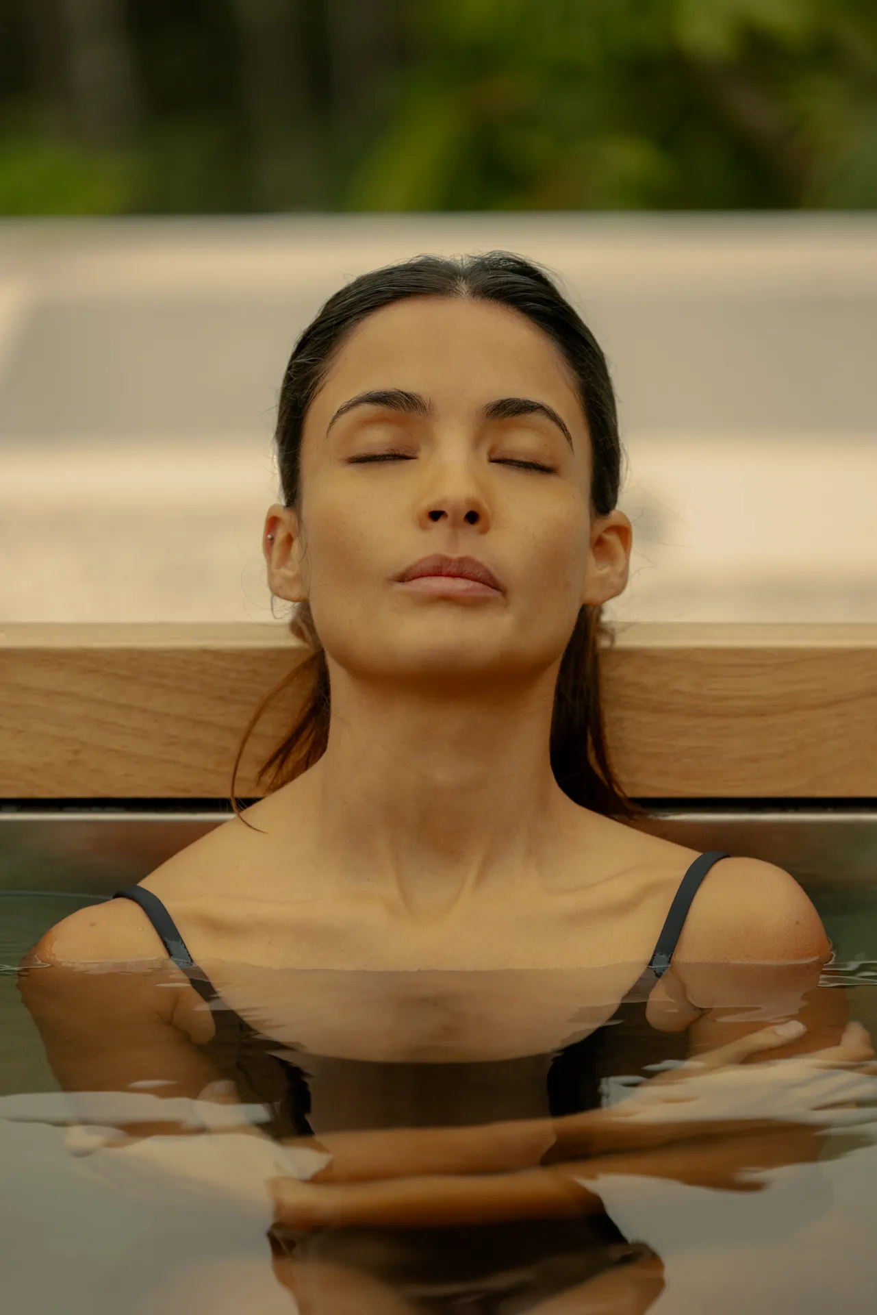 Woman with closed eyes relaxing in a pool with arms crossed just below water surface.