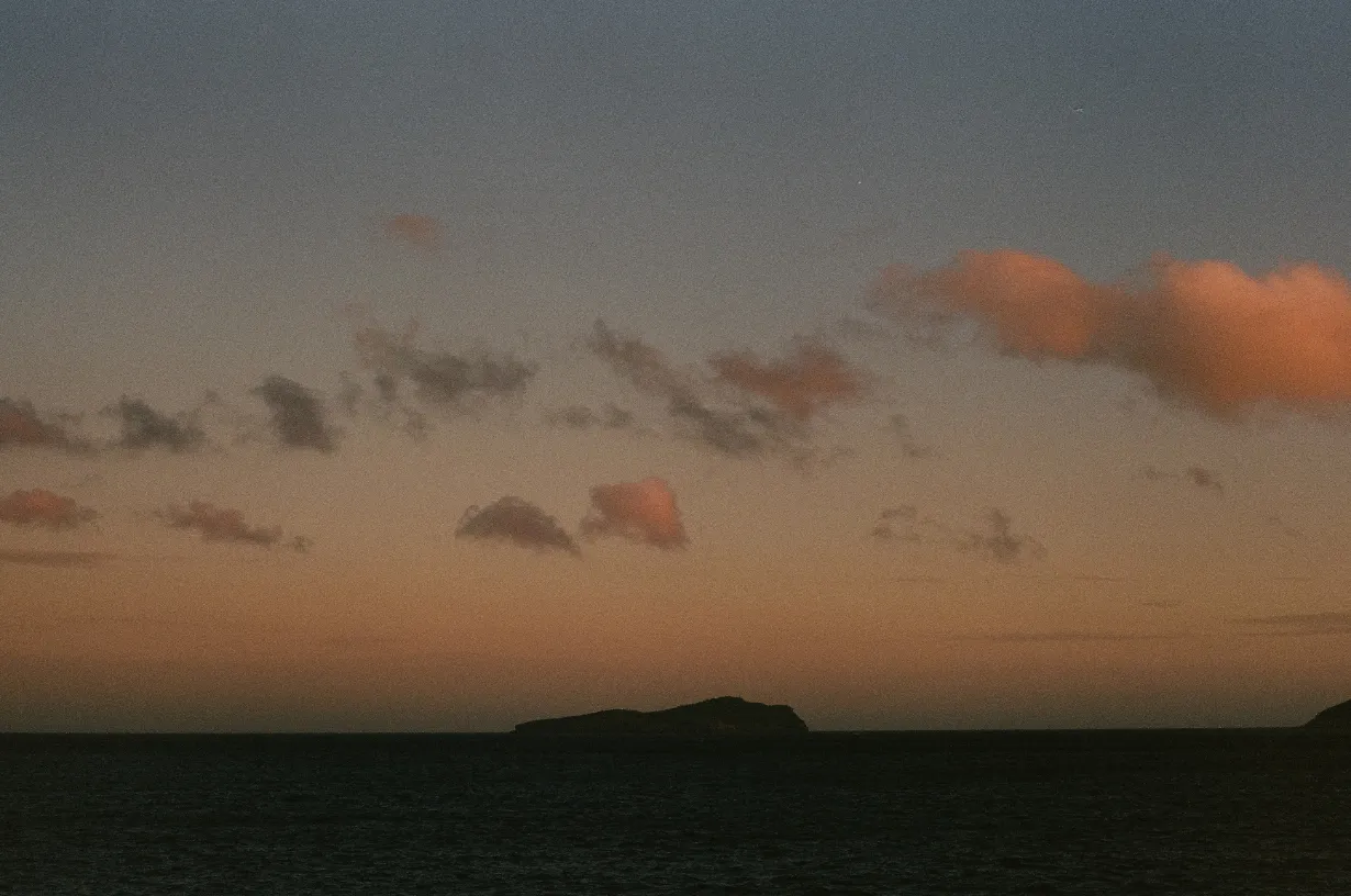 Island silhouette against a dark ocean under a twilight sky with scattered pink and gray clouds.
