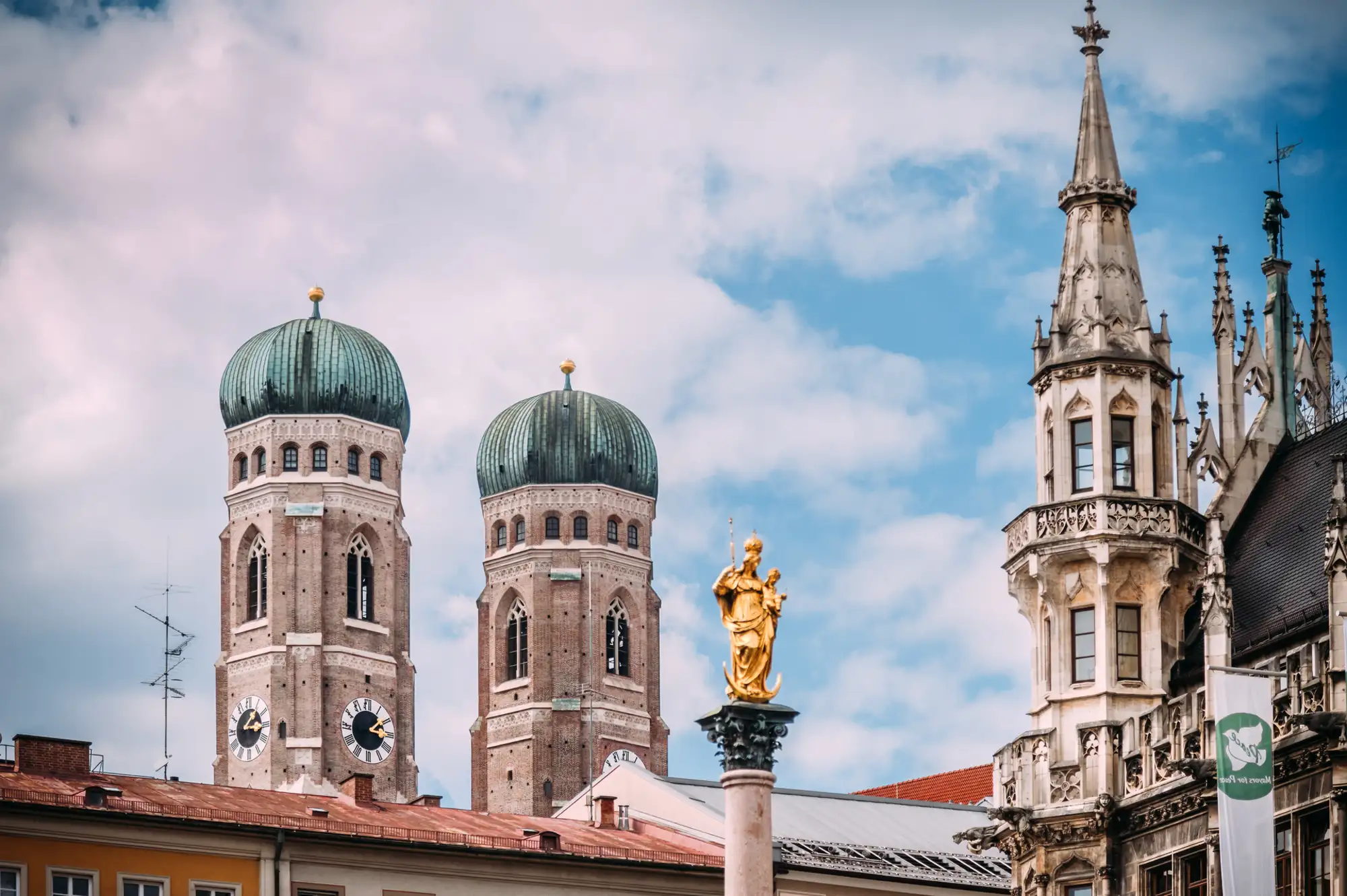 Blick über die Dächer des Münchner Marienplatzes, mit Marienstatue, Rathaustürmen und Frauenkirche.