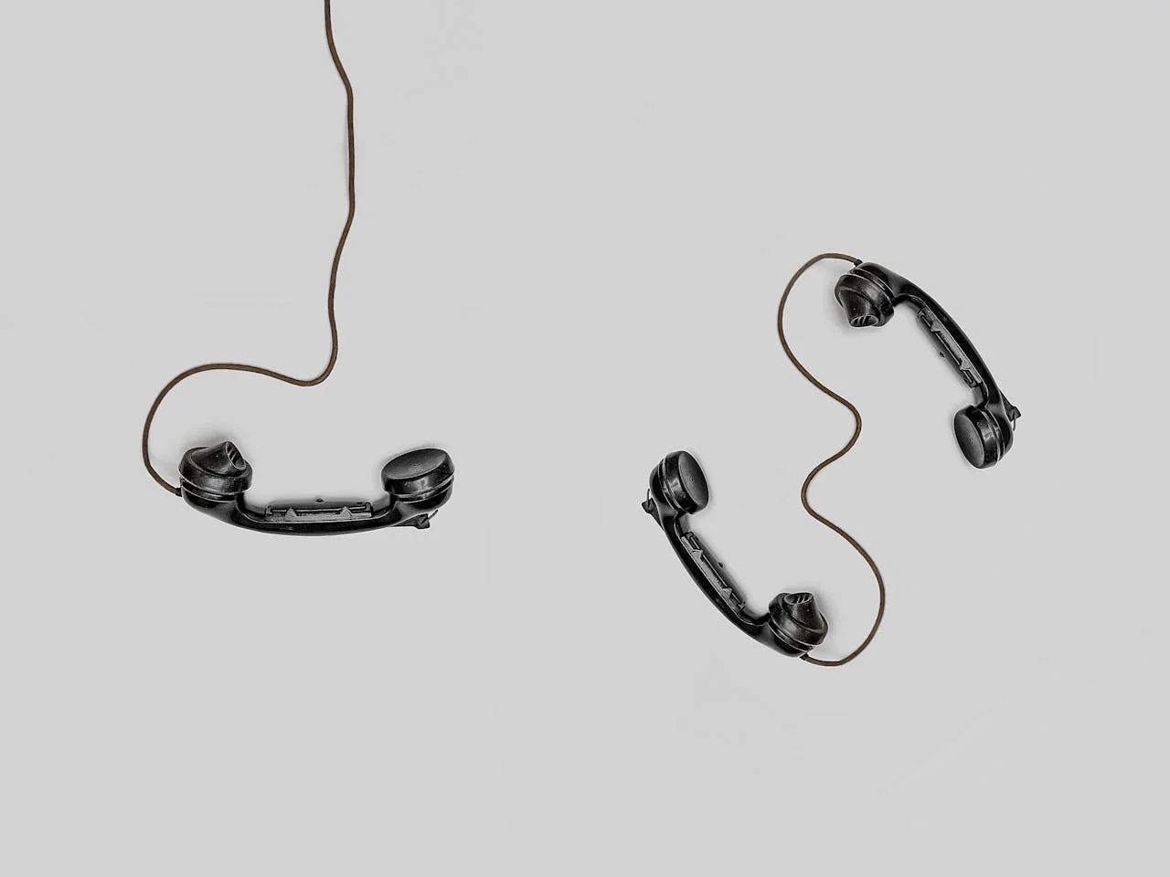 Three black vintage telephone handsets arranged on a light gray background with cords loosely connecting them.