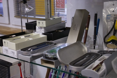 Display of boxed pens and pen cases on a glass shelf inside a store.