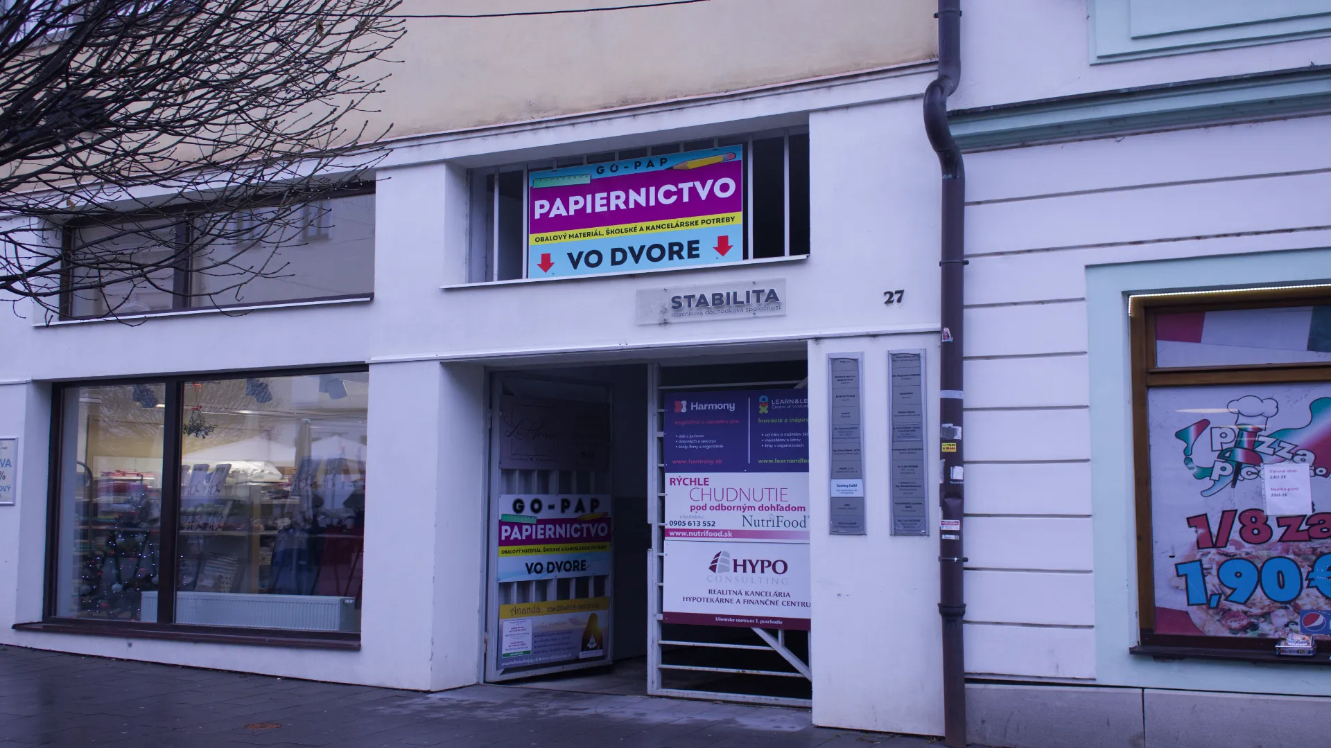 Commercial building entrance with signs for a stationery store, consulting services, and a pizza restaurant window.