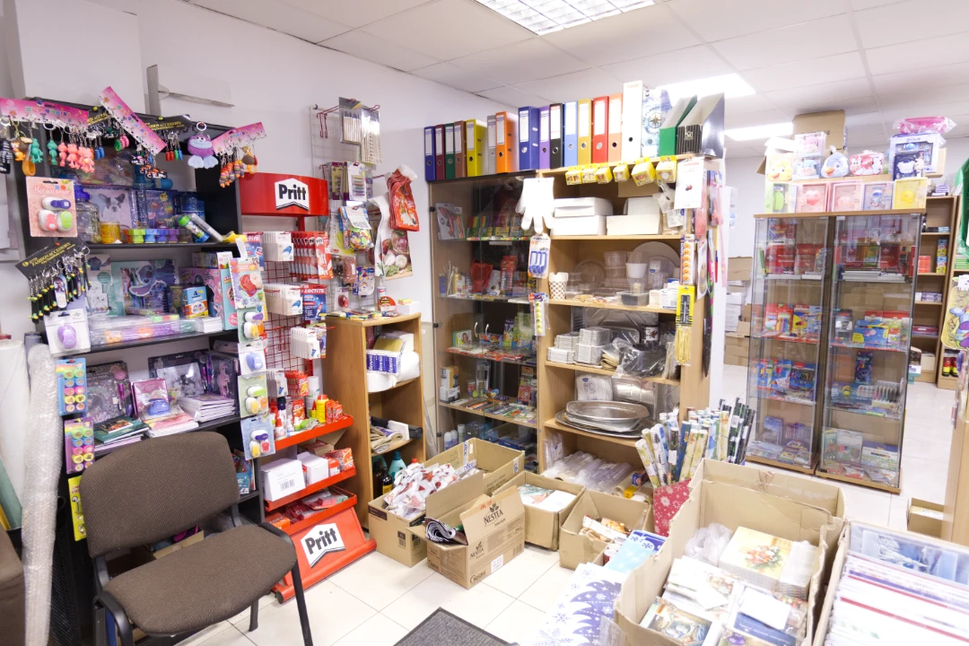 Interior of a well-lit stationery and gift shop with shelves and boxes filled with office supplies, wrapping paper, and small toys.