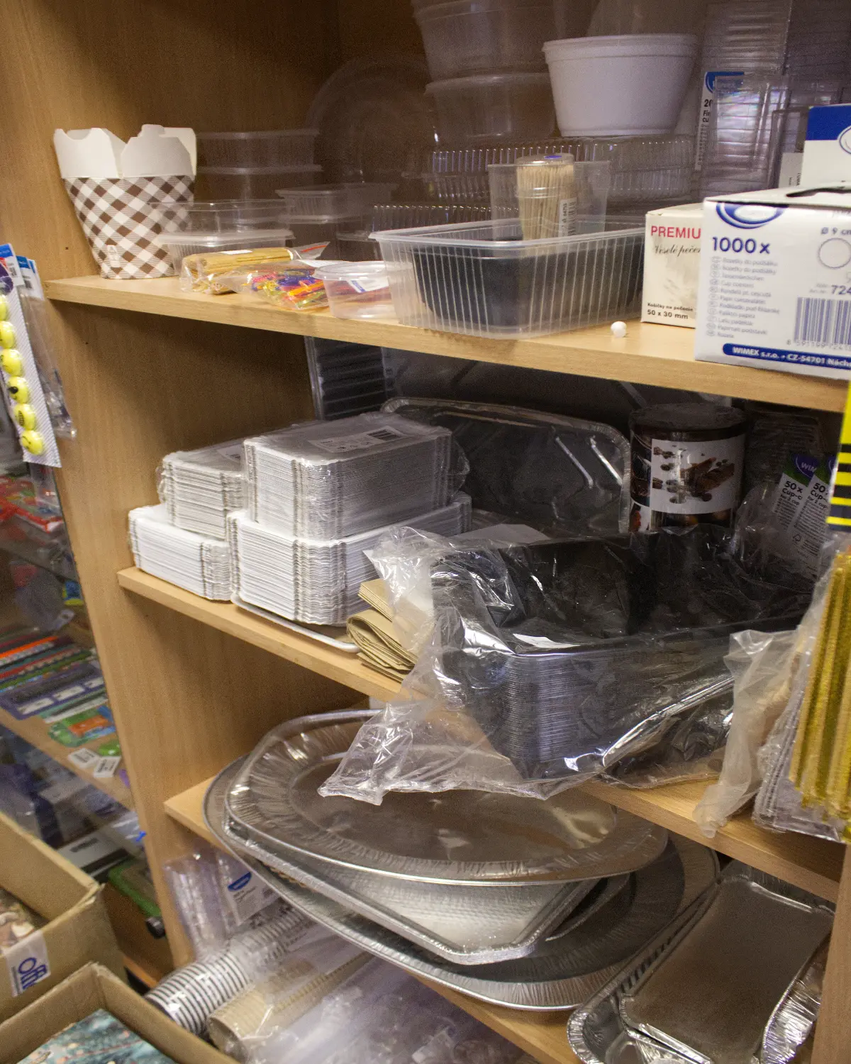 Wooden shelves stocked with various disposable plastic and aluminum food containers, trays, cups, and boxes.