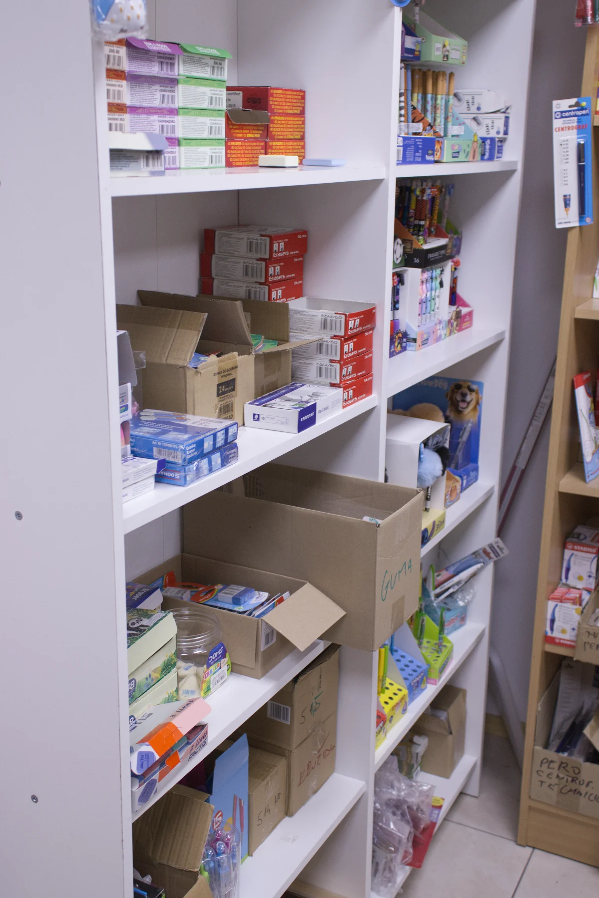 White shelves stocked with various boxed office supplies including erasers, pens, and other stationery items.