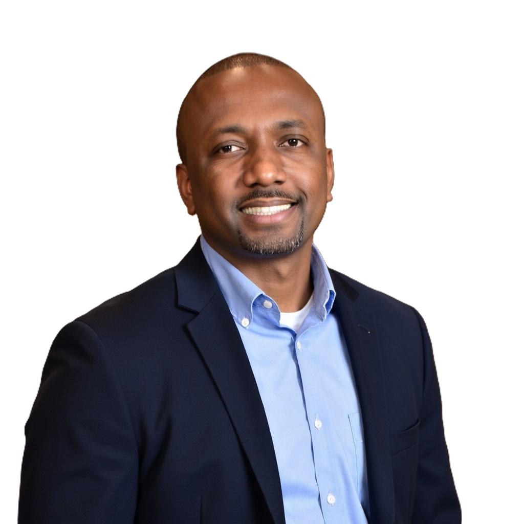 Dale man with short hair and goatee wearing a light blue shirt and dark blazer on white background.
