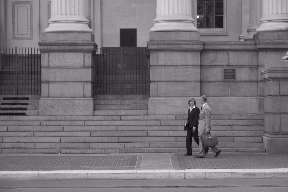 Two business professionals walking and talking in front of a building with large stone columns and steps.