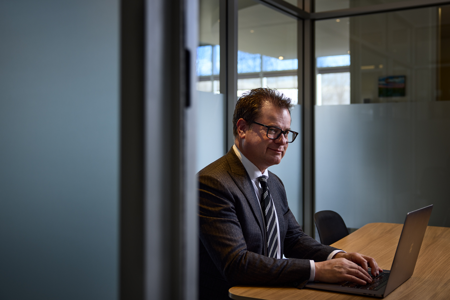 Lawyer Jason G. Debly working at a conference table in a private office at CLG Law, wearing glasses and a suit with striped tie.