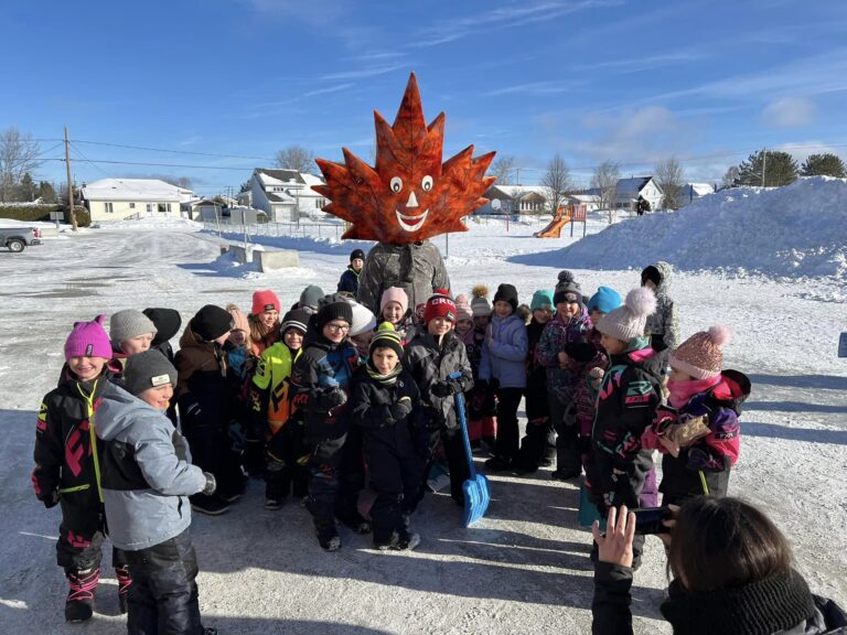Children gathered outdoors in winter with maple leaf mascot in New Brunswick community festival
