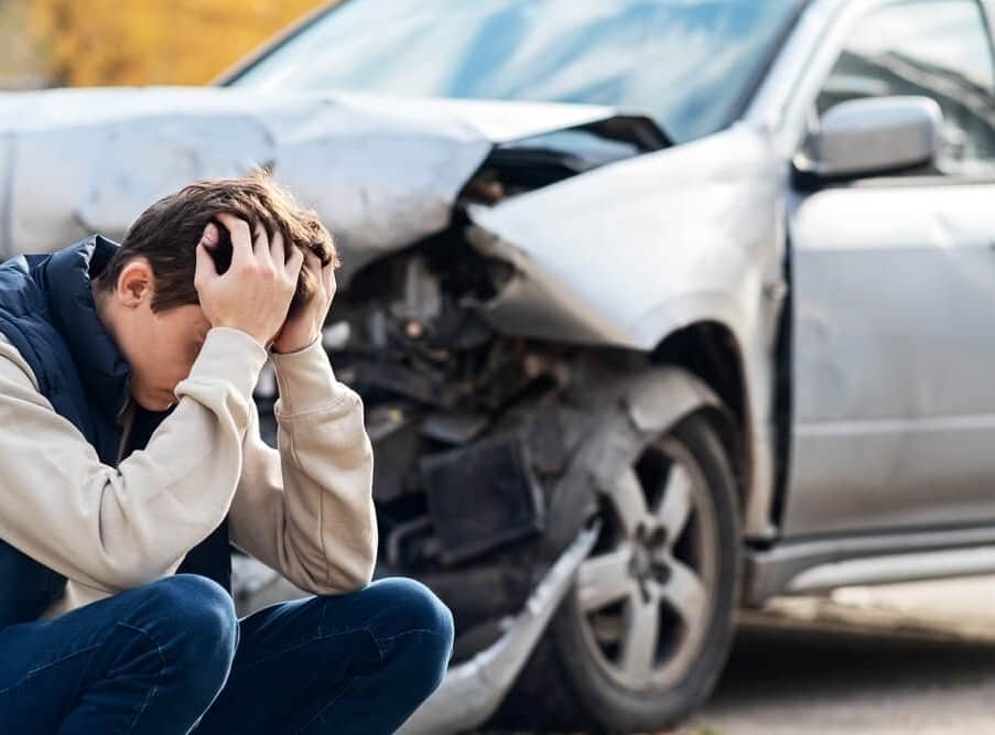 Man sitting in distress beside a heavily damaged car after a hit-and-run accident.