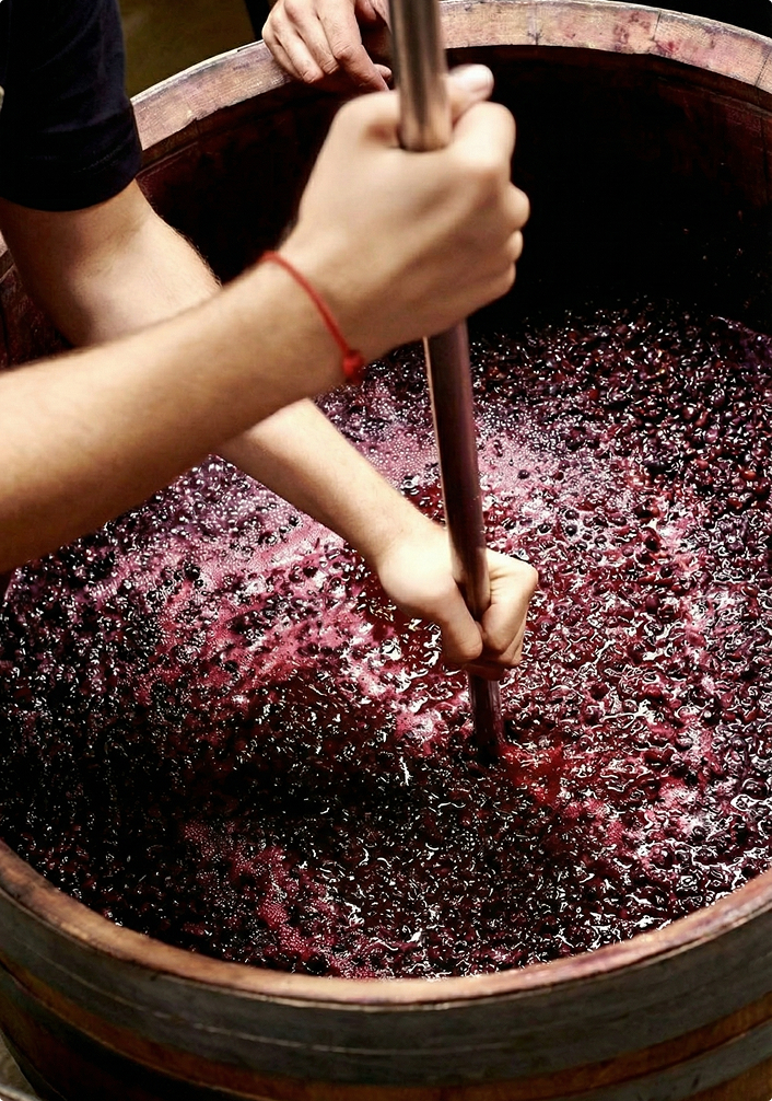 Hands stirring crushed grapes inside a wooden barrel during wine fermentation.