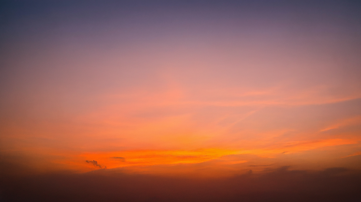 Sunset sky with gradient colors ranging from deep purple to bright orange above dark clouds.