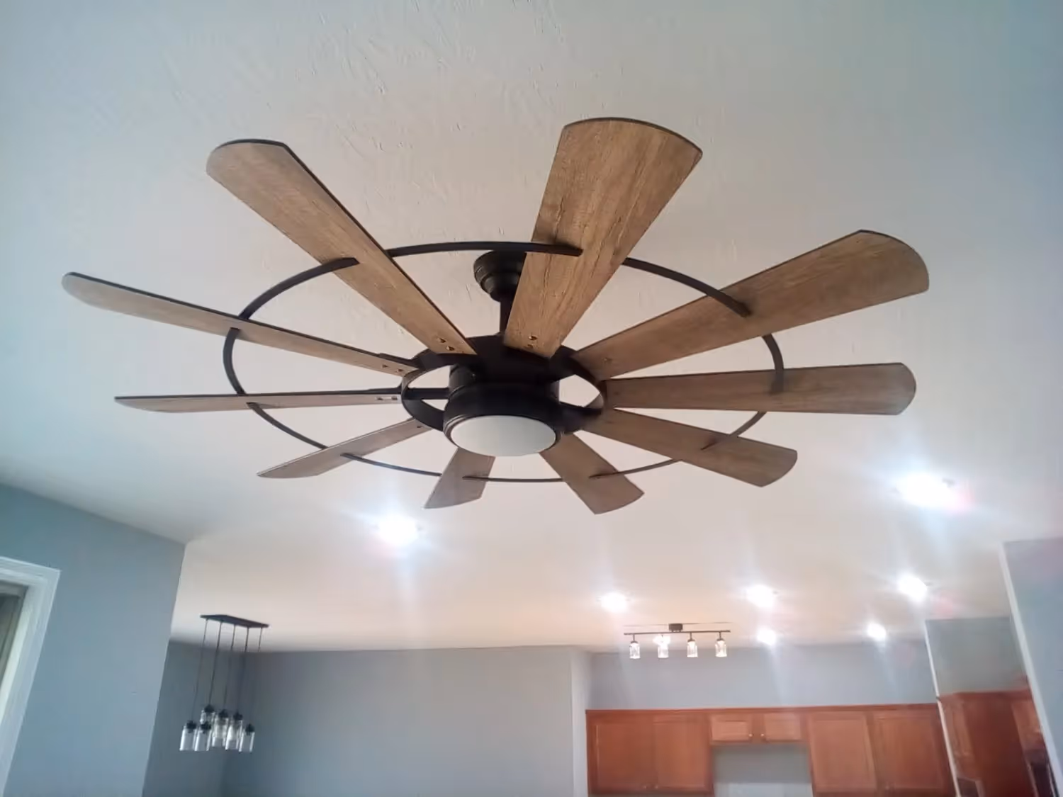 A modern ceiling fan with ten light-brown wooden blades and a circular metal frame mounted on a white ceiling.