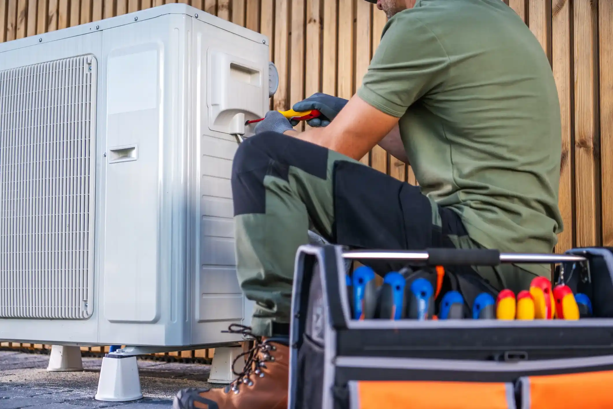 Close-up of an HVAC technician working on an outdoor air conditioning unit with tools in a toolbox.