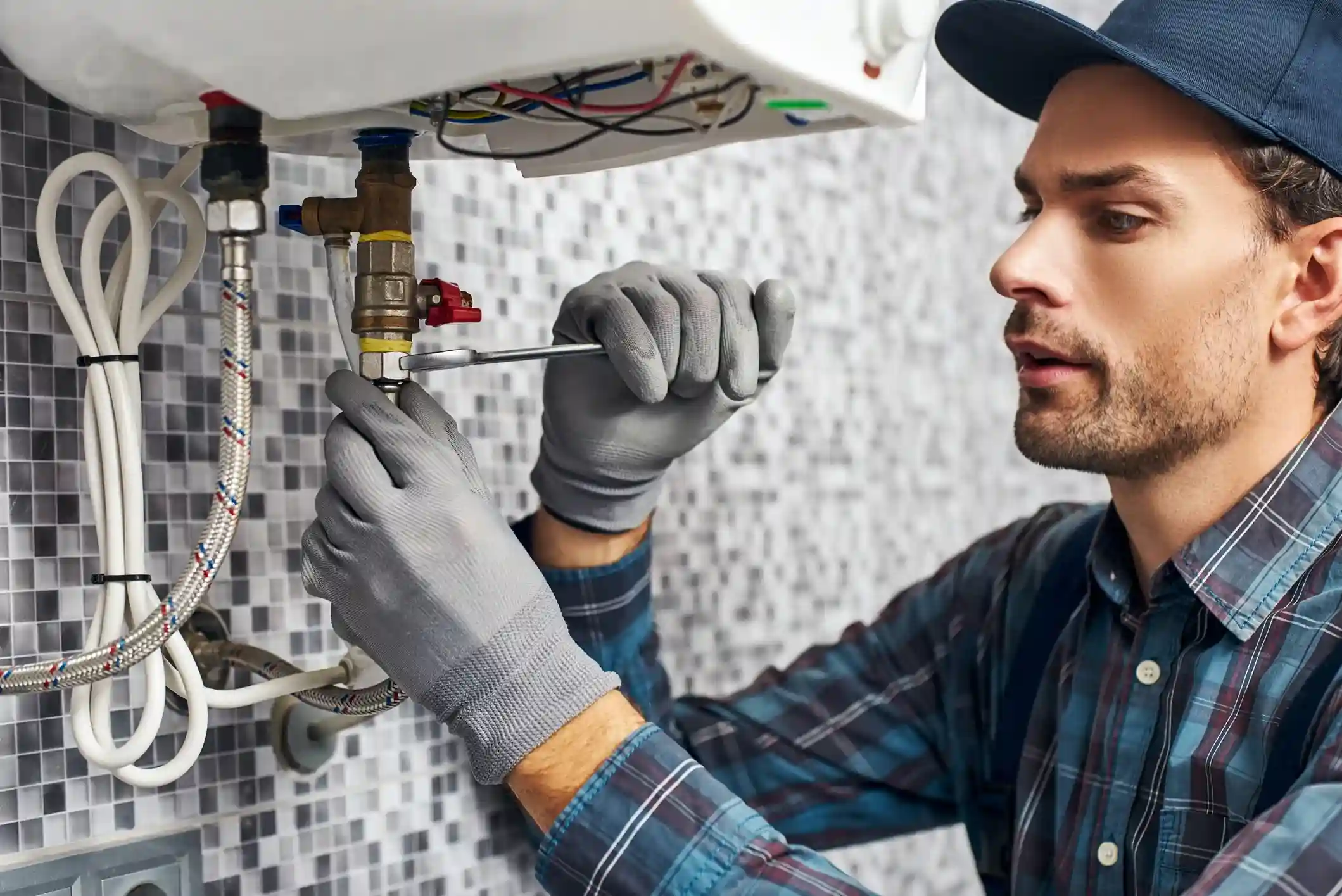 HVAC professional or plumber repairing a small water heater or boiler unit using a wrench.