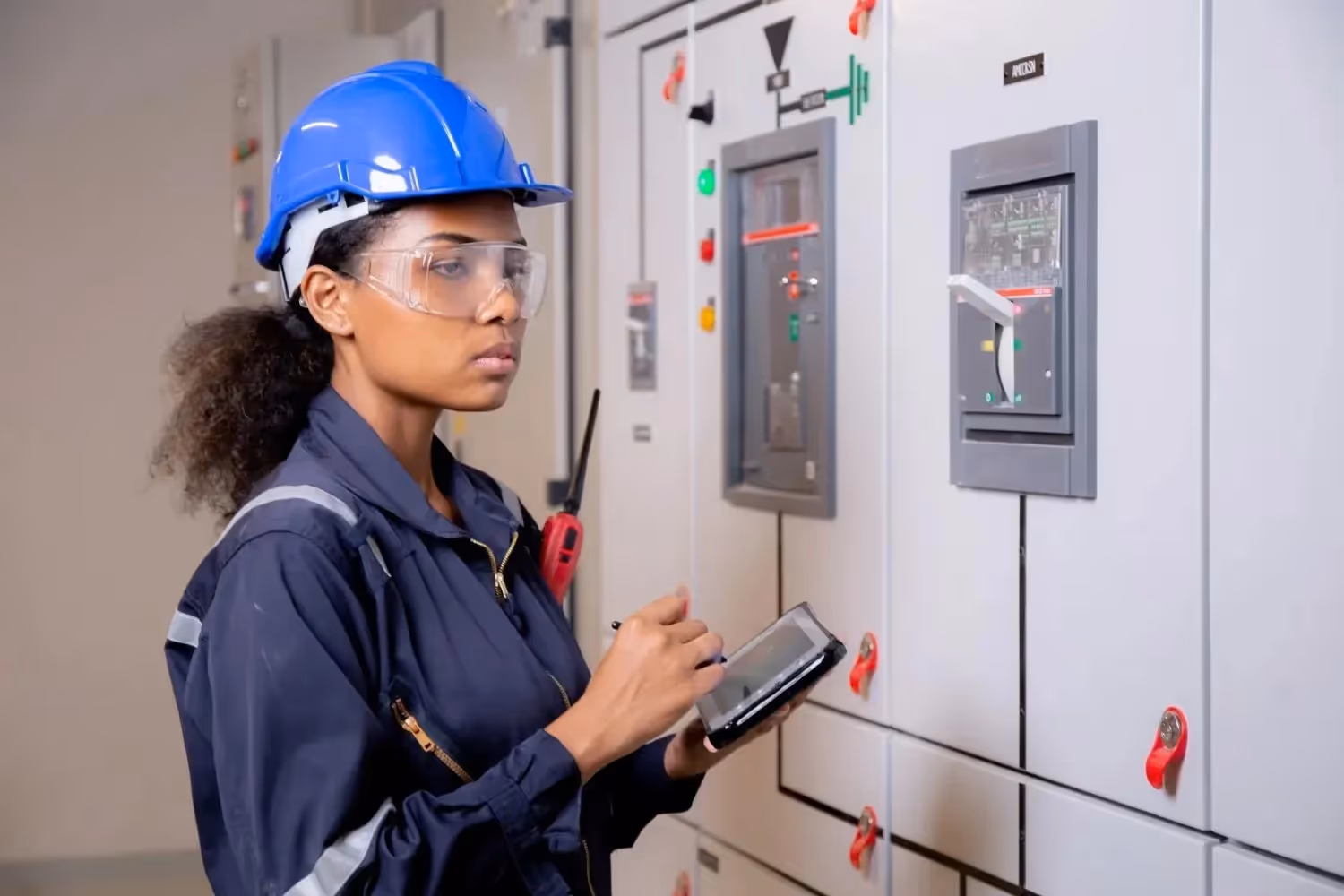 A technician in safety gear uses a digital tablet to conduct an energy inspection of an electrical power distribution panel.