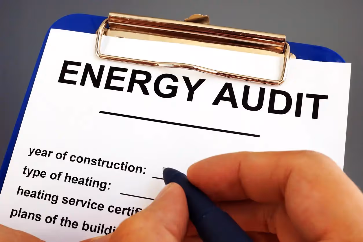 A hand holds a pen, poised to fill out an "Energy Audit" form on a clipboard. 