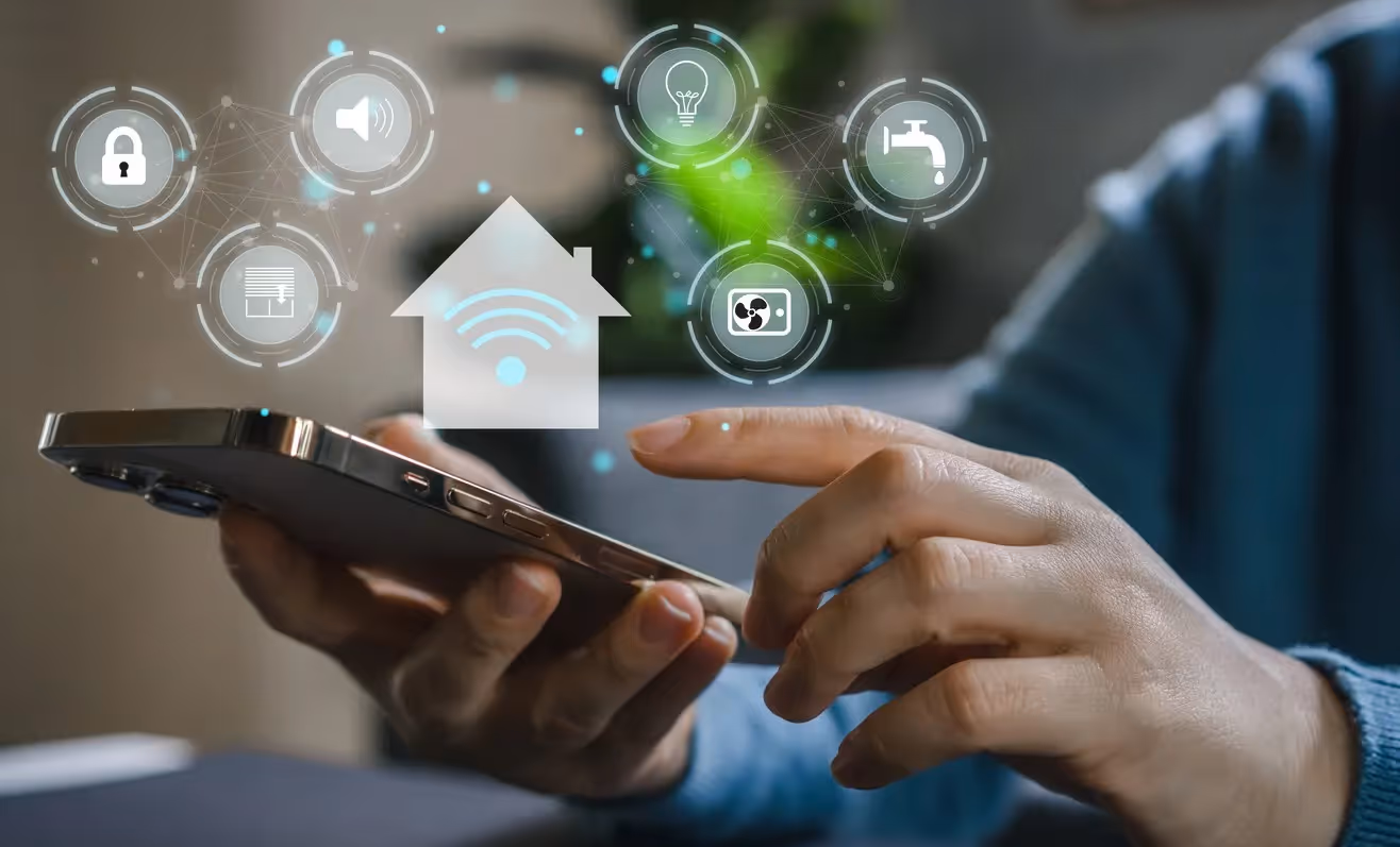 A close-up of hands holding a smartphone with digital smart home icons floating above it. These glowing icons include symbols for Wi-Fi, a light bulb, a lock, a faucet, and an air conditioning unit.