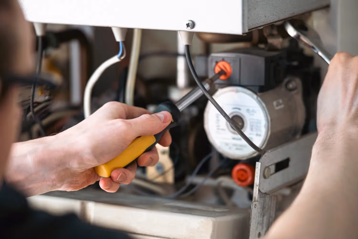 Technician uses screwdriver and wrench to adjust internal boiler components with visible wiring and motor.