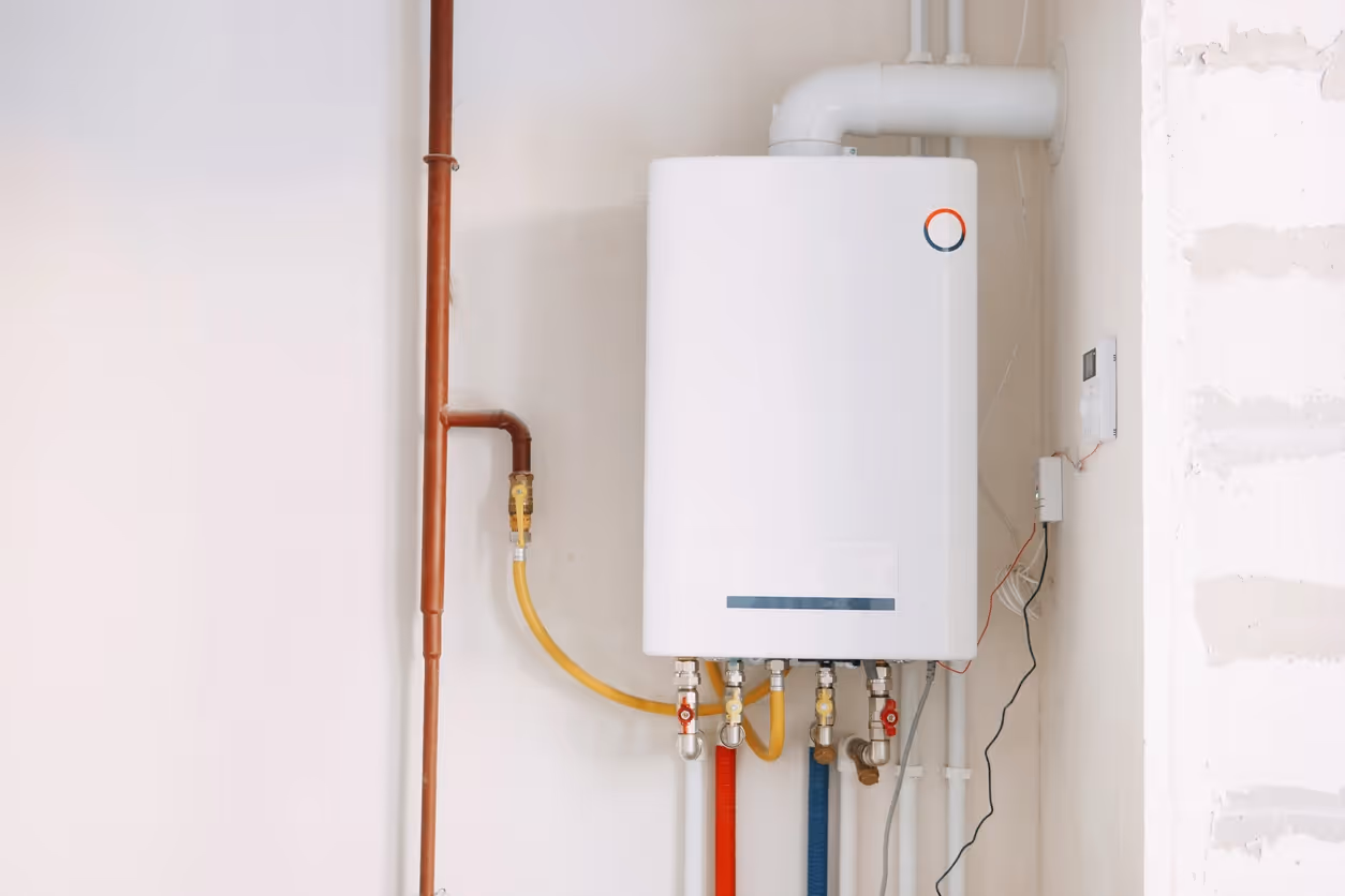 A white gas water heater is mounted on a wall. It has red, blue, and yellow pipes attached at the bottom