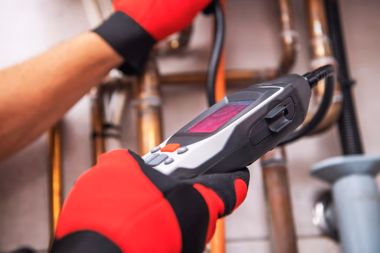A technician wearing red gloves uses an infrared thermometer to inspect pipes. 