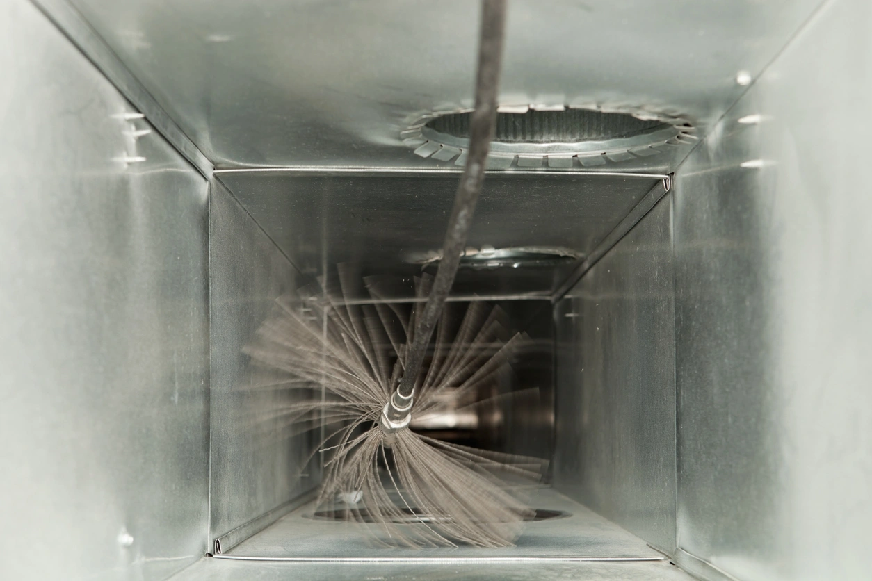 View inside a metal air duct with a rotating brush cleaning tool, creating a sense of motion and efficiency. 