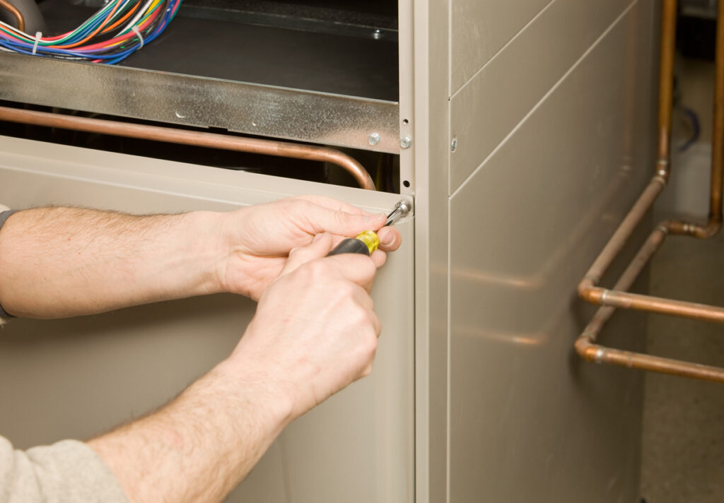 Hands using a screwdriver to repair a beige furnace.