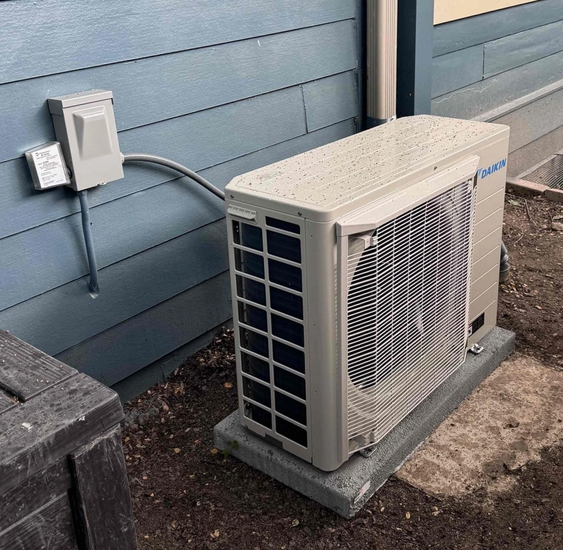 Outdoor air conditioning unit on a concrete slab against a blue wooden house exterior. 
