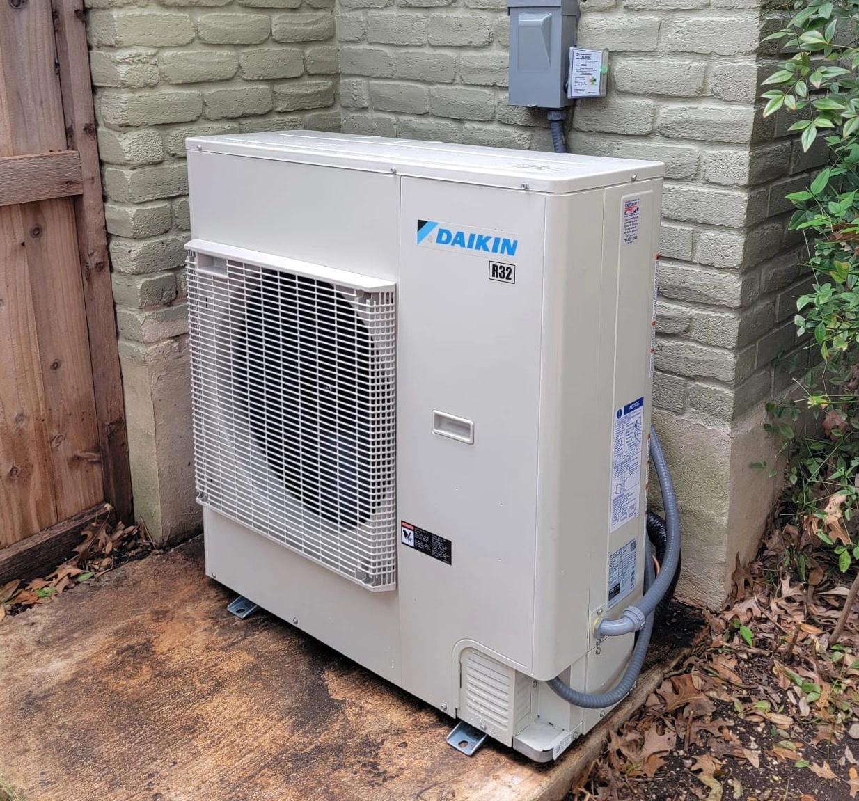 Outdoor air conditioning unit labeled "Daikin R32" with a protective grille