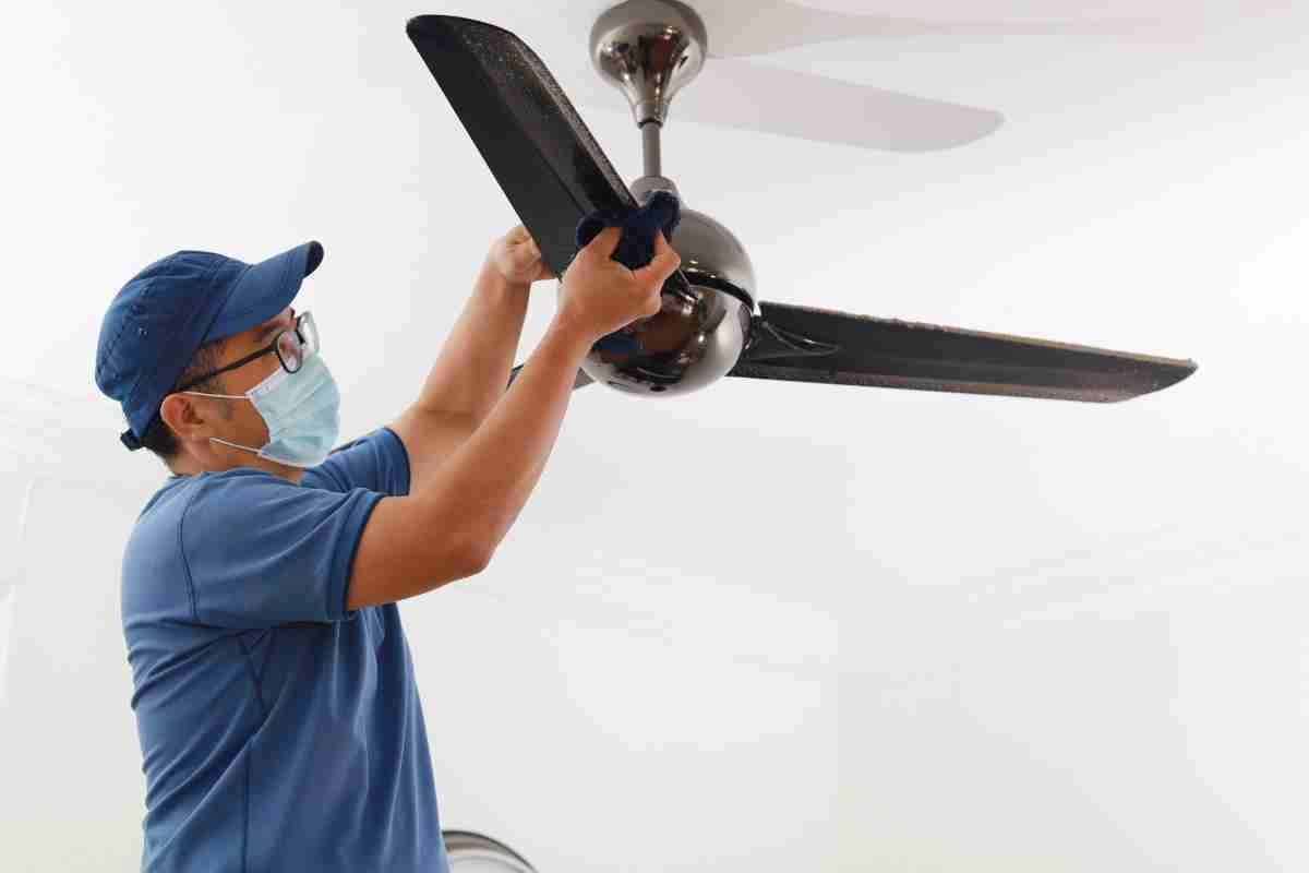 Masked man cleaning black ceiling fan.