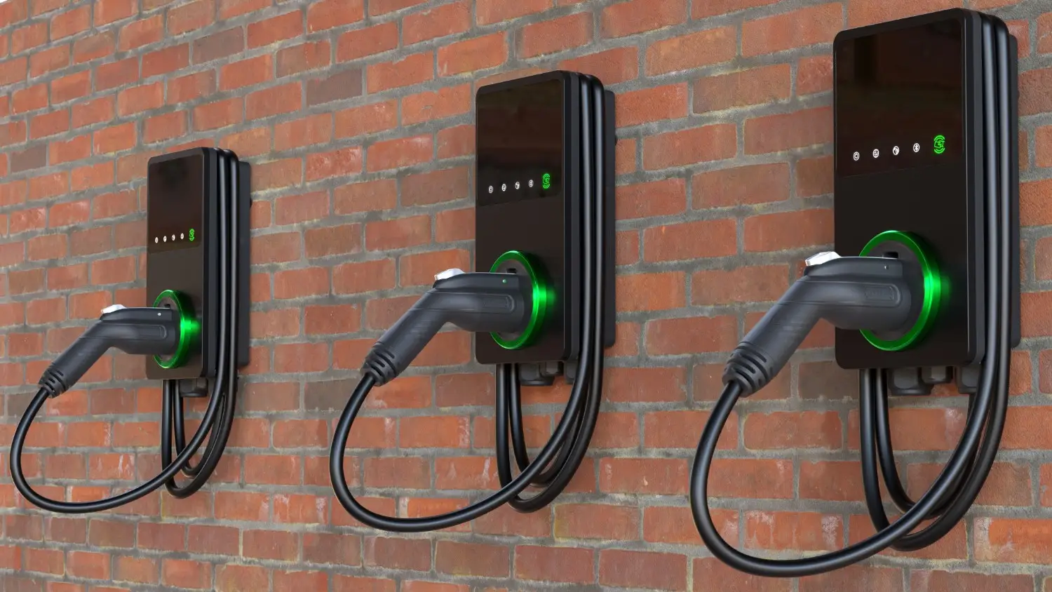 Three electric vehicle charging stations mounted on a brick wall with green illuminated indicators and plugged-in charging cables.