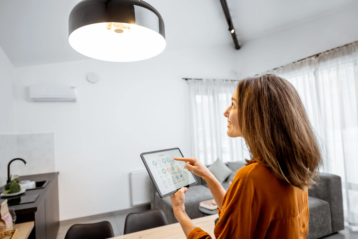 A woman using a tablet to control smart home devices in a modern living room. 