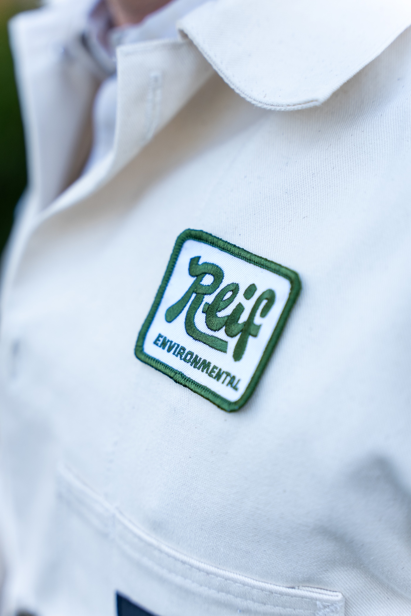 Close-up of a white jacket with a green-bordered patch reading 'Reif ENVIRONMENTAL'.