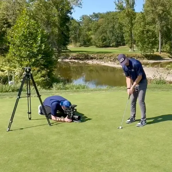 A cameraman shooting video of a golfer in the process of making a putt. 