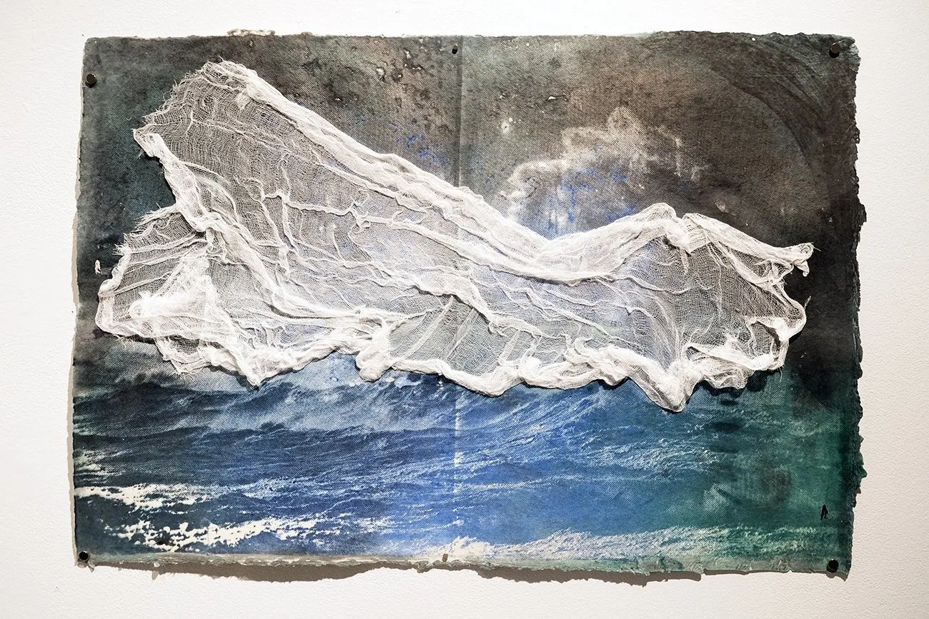 Blue and purple artwork False Dawn on gallery wall with ocean motif, collaged with cheesecloth depicting turbulent ocean with immigrant boats, Nazanin Noroozi.