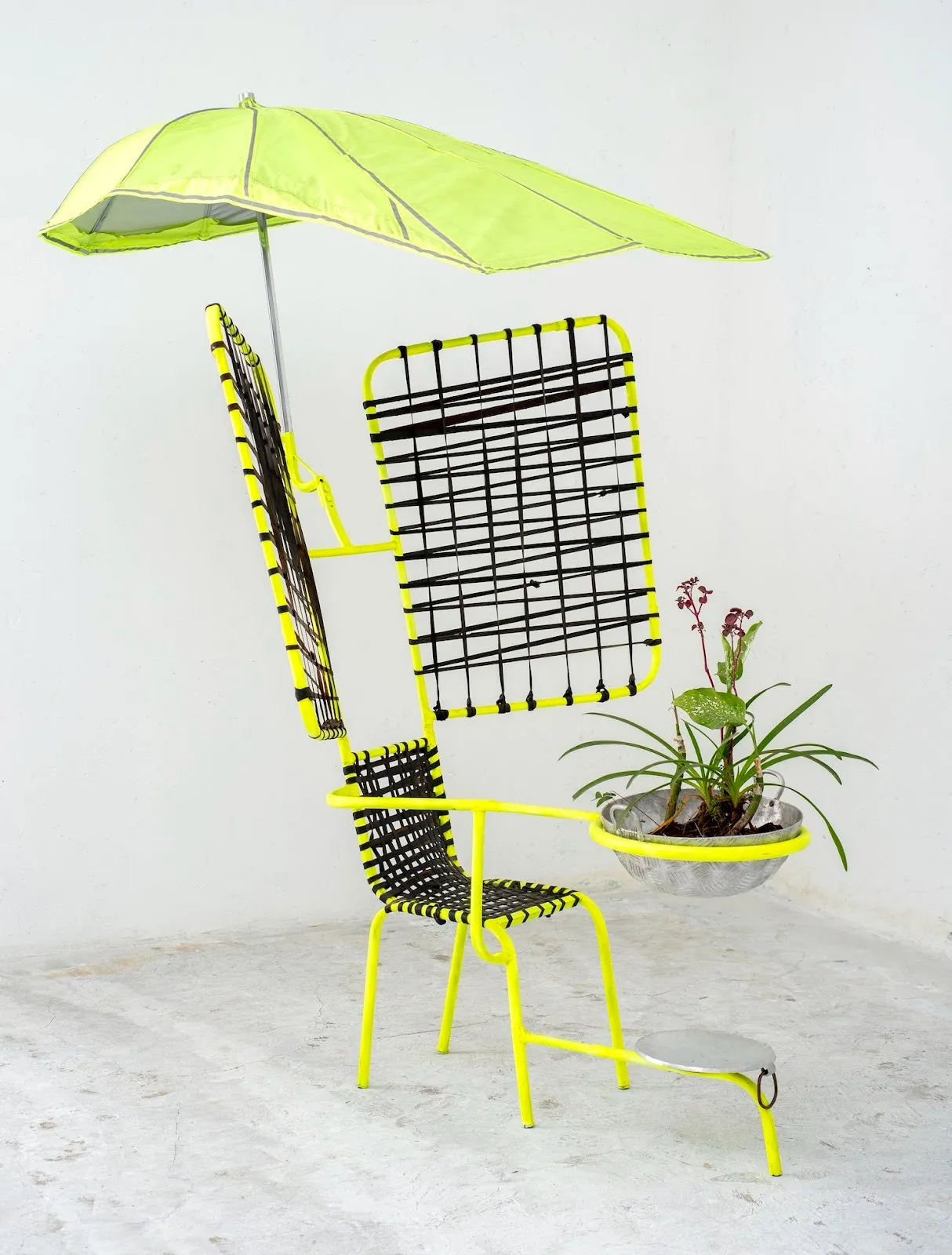 Neon yellow and green chair installation with welded metal protrusions and black tennis net as decoration, pot of plants in front of armrest, utopia chair sculpture by Ajax Axe from Kairos Futura.