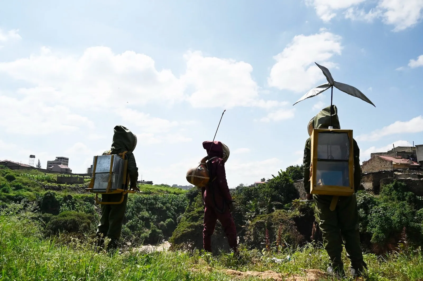 Kairos Futura team members shooting a short film at one of the Micro-Utopia locations, The Temple in Lucky Summer, men in protection suits with windmill attached to backpack walking on grass field.