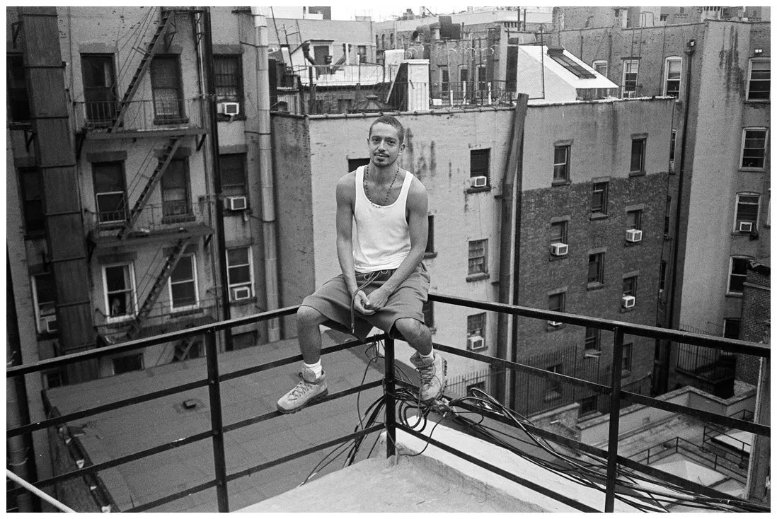 Guatemalan American artist Gio Black Peter sitting on top of handrails, rooftop Chinatown New York, wearing white tank top, queer visual artist, actor, musician, courtesy of Waltpaper.